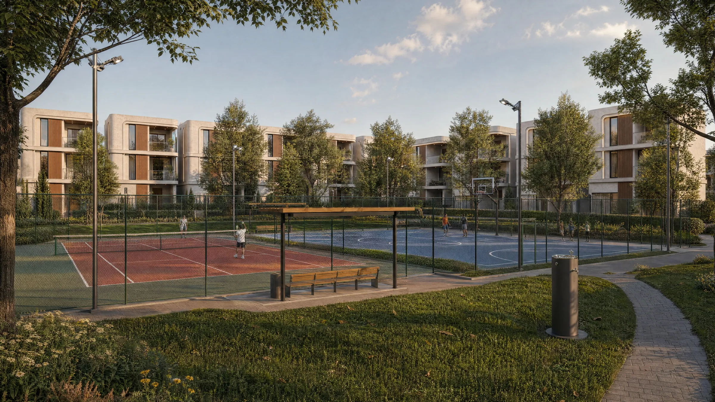 Tennis court and a blue multipurpose court in a park, with a shaded bench and villas behind the trees
